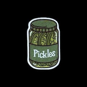 May include: An embroidered patch shaped like a glass jar filled with green pickles. The jar features a dark green label with the white text Pickles written in a cursive font. The entire design is outlined with a thick white border.