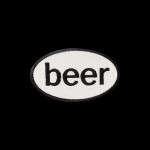 May include: An oval-shaped embroidered patch featuring a white background with a black border. The word beer is stitched in lowercase black letters across the centre of the patch. The design is simple and clear with a textured fabric appearance.
