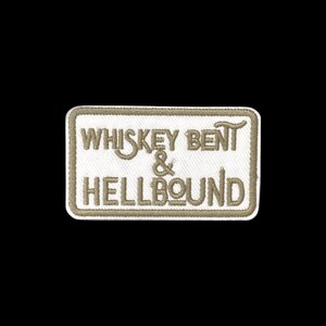 May include: A rectangular embroidered patch with a white background and a tan border. The text "WHISKEY BENT & HELLBOUND" is stitched in tan thread across the centre in a stylised, bold font, featuring a rounded rectangular shape.