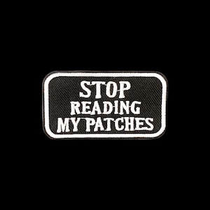 Peut inclure: Un écusson rectangulaire brodé avec un fond noir et une bordure blanche. Le texte STOP READING MY PATCHES est cousu en lettres capitales blanches au centre de l'écusson. Le design présente une finition en tissu texturé.