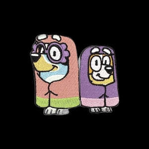 May include: Two embroidered patches featuring cartoon dog characters. The larger character wears purple glasses and a pink and green hooded cloak. The smaller character is wrapped in a purple and pink hooded cloak. Both have white and tan faces.