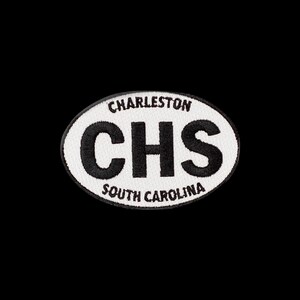 May include: An oval-shaped embroidered patch featuring a white background with a black border. The text CHARLESTON is arched at the top, the letters CHS are centered in large black font, and SOUTH CAROLINA is arched at the bottom in black.