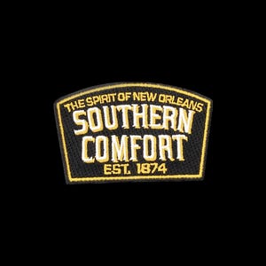 May include: A black embroidered patch with a curved top edge featuring the yellow and white text THE SPIRIT OF NEW ORLEANS SOUTHERN COMFORT EST. 1874. The patch has a thick yellow border and a black background with detailed stitching throughout.
