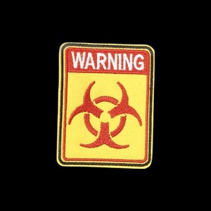 May include: A rectangular embroidered patch featuring a yellow background with a red biohazard symbol in the centre. The top section contains the word WARNING in white capital letters on a red rectangular background with a black border.