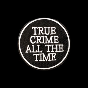 Pode incluir: Um emblema bordado circular com fundo preto e borda branca. O texto "TRUE CRIME ALL THE TIME" está bordado em letras maiúsculas brancas no centro do emblema, disposto em quatro linhas com um estilo de fonte claro e em negrito.