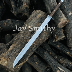 May include: A long, silver bladed sword with a wooden handle and a silver guard. The sword rests on a pile of dark brown logs. The text "Jay Smithy" is visible on the logs.