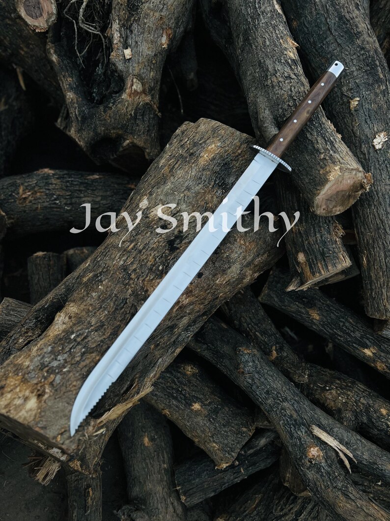 May include: A long, silver bladed sword with a wooden handle and a silver guard. The sword rests on a pile of dark brown logs. The text "Jay Smithy" is visible on the logs.