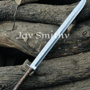May include: A large, silver sword with a serrated edge and a wooden handle. The handle is dark brown with silver accents. The text "Jay Smithy" is visible on the surface.