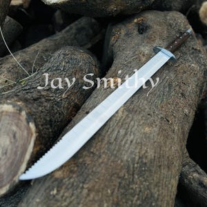 May include: A large, silver sword with a serrated edge and a dark brown handle rests on a pile of wooden logs. The text "Jay Smith" is visible in the image.