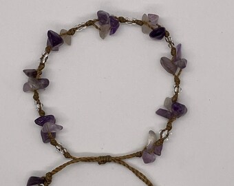 May include: A brown cord bracelet with purple and clear stones.