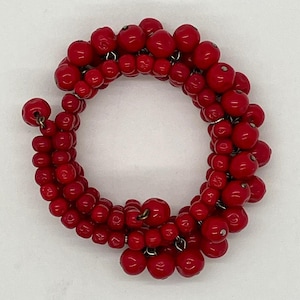 May include: A circular red beaded bracelet. The bracelet is made of small, round, red beads strung together. The beads are a vibrant red color and are arranged in a dense, circular pattern. The bracelet is likely a fashion accessory.