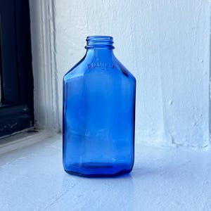 May include: A cobalt blue glass bottle with a rounded top and a hexagonal body. The bottle has a label that reads "SQUIBB & SONS, NEW YORK".