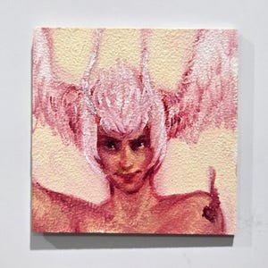 Puede incluir: Pintura cuadrada que presenta un retrato de una persona con cabello y alas rosas. La obra de arte utiliza una paleta de colores rosa y crema. El sujeto tiene una expresión severa. La pintura está montada sobre una superficie blanca.