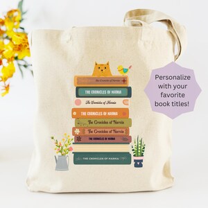 May include: Beige tote bag featuring a stack of illustrated books with the title "The Chronicles of Narnia." A cartoon cat and bird sit atop the books. The bag also has a small watering can and potted plants. Text on the bag says "Personalize with your favorite book titles!"