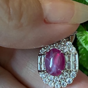 May include: A pink star ruby gemstone set in a silver ring with a halo of smaller diamonds.