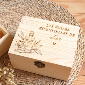 Peut inclure: Une boîte rectangulaire en bois clair avec un fermoir en métal. Le couvercle présente une gravure au laser représentant une bouteille et des plantes, ainsi que le texte "LES HUILES ESSENTIELLES DE Lisa" et un petit cœur. Bois au grain naturel.