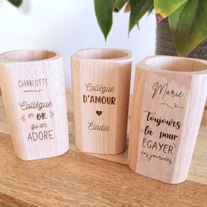 Peut inclure: Trois porte-crayons en bois avec des messages gravés. Le premier porte-crayon dit "Charlotte Collègue en OR qu'on ADORE". Le deuxième porte-crayon dit "Collègue D'AMOUR Élodie". Le troisième porte-crayon dit "Marie Toujours là pour ÉGAYER nos journées".