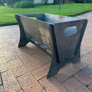 May include: A metal fire pit with a rectangular shape and a handle on one side. The fire pit is sitting on a brick patio.