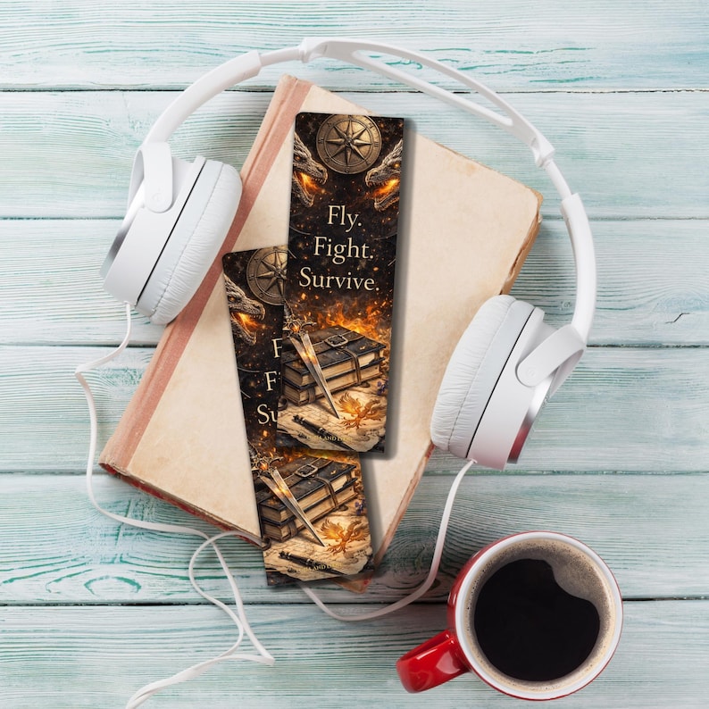 May include: Two bookmarks with the text "Fly. Fight. Survive." are displayed on a book, next to a pair of white headphones and a red coffee mug. The bookmarks feature a compass, dragon heads, and a stack of books.