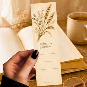 May include: A rectangular cream-colored paper bookmark featuring a botanical illustration of wheat stalks and leaves at the top. The text reads Today, I am grateful for... followed by three horizontal lines for writing. The brand name LUNA AND LOM is printed at the bottom.