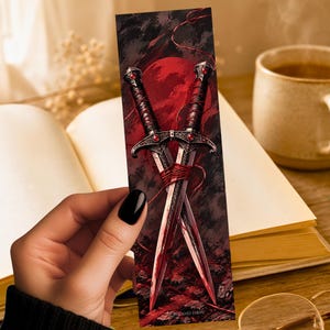 May include: A rectangular bookmark featuring a dark, atmospheric illustration of two crossed daggers with ornate silver hilts and red gemstone accents. The blades are wrapped in thin red thread against a backdrop of a large, glowing red moon.