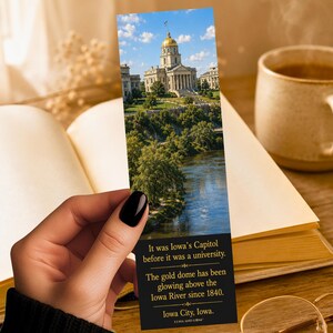 May include: A rectangular bookmark featuring a photograph of the Iowa State Capitol building with a gold dome above the Iowa River. The bottom section is black with gold text: It was Iowa's Capitol before it was a university. The gold dome has been glowing above the Iowa River since 1840. Iowa City, Iowa. LUNA AND LOOM.