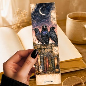 May include: A rectangular bookmark featuring a watercolor illustration of three black ravens perched on a stone wall under a crescent moon and starry night sky. Below the wall are vintage books, a crystal, and an ink bottle. Text reads LUNA AND LOOM.