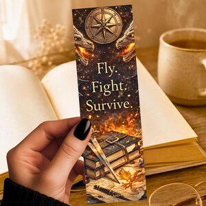 May include: A fantasy bookmark with a compass, dragons, and the text "Fly. Fight. Survive." The bookmark has a detailed illustration of books, swords, and a phoenix. The colour palette includes gold, brown, and orange.