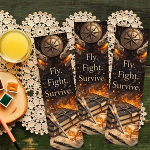 May include: Three fantasy-themed bookmarks with a compass, dragon heads, and the text "Fly. Fight. Survive." Each bookmark features a sword, books, and a map. The background is dark with flames.
