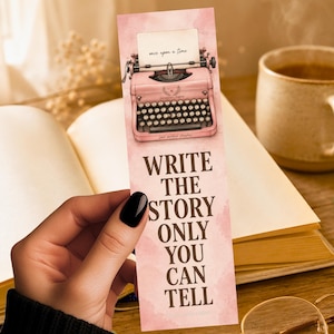 May include: A rectangular paper bookmark with a pink watercolor background featuring an illustration of a vintage pink typewriter at the top. The typewriter paper reads "once upon a time." Below, the text reads "WRITE THE STORY ONLY YOU CAN TELL."