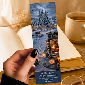May include: A bookmark featuring a winter scene of a snowy village with a bistro and a pond. The bookmark has the text "In Three Pines the light is always on." and the author's name. The bookmark is held over an open book.