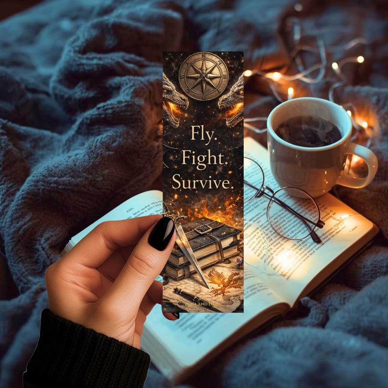 May include: A fantasy bookmark with the words "Fly. Fight. Survive." features a compass and dragon heads. The bookmark is held over an open book, with a cup of coffee and glasses in the background. The bookmark has a sword and a book illustration.