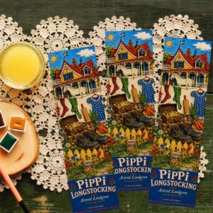 Op de afbeelding: Drie boekenleggers met illustraties uit de Pippi Langkous-boekenserie. Elke boekenlegger toont een kleurrijke sc&egrave;ne met een huis, paarden en diverse objecten. De tekst "Pippi Langkous" en de naam van de auteur zijn zichtbaar.