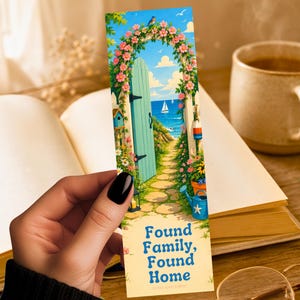 May include: A rectangular bookmark featuring a colorful illustration of a light blue door opening to a coastal path with pink flowers, a blue bird, a sailboat, and a blue watering can. The text reads Found Family, Found Home in blue letters.