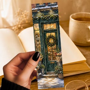 May include: A rectangular bookmark featuring a detailed illustration of a dark green storefront entrance during winter. The scene includes a festive wreath on the glass door, snow-covered ground, evergreen garlands, and potted plants, all illuminated by warm lights.
