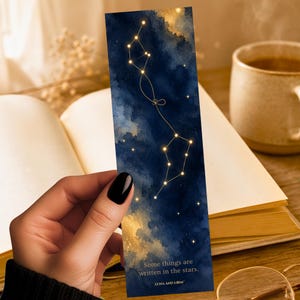 May include: A rectangular bookmark featuring a deep blue and gold watercolor night sky background with a connected constellation pattern. The text reads, "Some things are written in the stars." and "LUNA AND LOOM" is printed at the bottom.