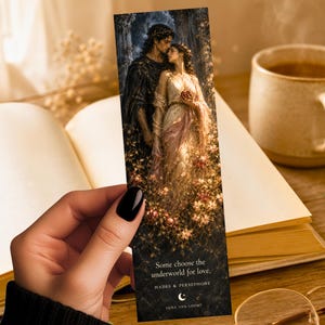 May include: A rectangular bookmark featuring a dark, detailed illustration of Hades and Persephone standing amidst flowers. The text reads: Some choose the underworld for love. HADES & PERSEPHONE, with a crescent moon icon and the brand name Luna and Loom.