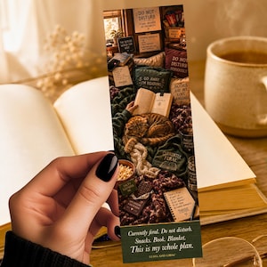 May include: A bookmark featuring a cozy reading scene with a cat, books, and snacks. The bookmark has the text "Currently feral. Do not disturb. Snacks. Book. Blanket. This is my whole plan."