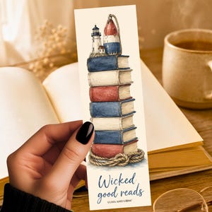 May include: A rectangular bookmark featuring a stack of books in red, white, and blue. At the top sits a lighthouse and a buoy. A rope wraps around the base of the stack. The text reads Wicked good reads and LUNA AND LOOM at the bottom.