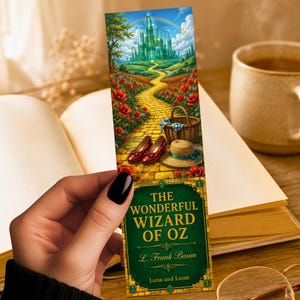 May include: A rectangular bookmark featuring a vibrant illustration of a yellow brick road leading to a green castle, red poppies, a woven basket, and red shoes. The lower section displays the text The Wonderful Wizard of Oz by L. Frank Baum.