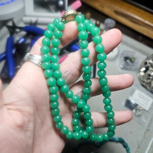 May include: A double strand necklace made of green jade beads. The necklace has a gold clasp.