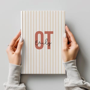 May include: A hardcover notebook featuring a vertical striped pattern in beige and white. The center displays the large, bold, terracotta-colored letters OT with the name Emily written in a black cursive script layered over the letters.