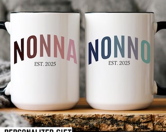 May include: Two white ceramic mugs with black handles and rims. One mug reads "NONNA EST. 2025" in brown and pink lettering. The other mug reads "NONNO EST. 2025" in blue, gray, and teal lettering. The words "PERSONALIZED GIFT" are at the bottom.