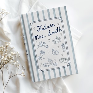 May include: A hardcover book with a blue and white striped cover. The cover features the text "Future Mrs. Smith" in cursive, along with line drawings of wedding-related icons, such as rings, shoes, and flowers.