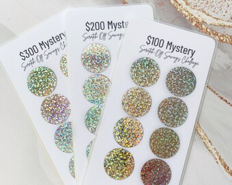 May include: Three cards with a holographic glitter finish. Each card has a different amount: $300, $200, and $100. The cards are labeled "Mystery Scratch Off Savings Challenge".