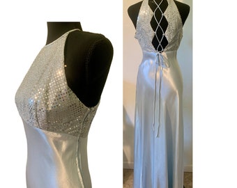 May include: A pale blue evening gown with a halter neckline and a flowing skirt. The bodice is embellished with silver sequins, and the back has a crisscross lace-up detail. The dress is displayed on a black mannequin.