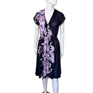 May include: A navy blue wrap dress with a V-neck and short sleeves. The dress features a floral pattern in shades of purple and white on the left side and down the front. The dress is knee-length and has a tie at the waist.
