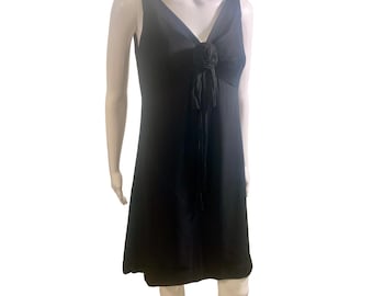 May include: A black sleeveless dress with a V-neckline and a floral embellishment at the bust. The dress has a fitted bodice and a slightly flared skirt. The dress is displayed on a mannequin.