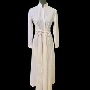 May include: A white long-sleeved dress with a high collar and a tie at the waist.