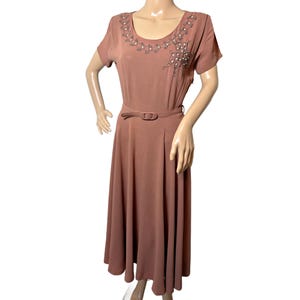 May include: A dusty rose midi dress featuring short sleeves, a round neckline, and a matching belt at the waist. The bodice is decorated with an embroidered vine pattern accented with small white beads along the collar and chest area.